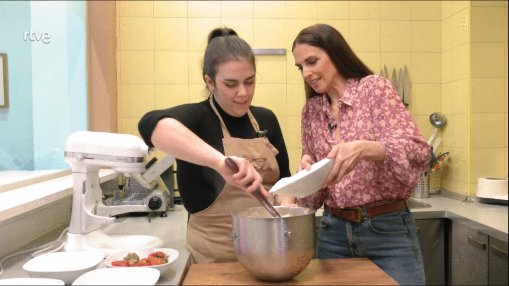 Momento del programa Sabores de Tierra de RTVE grabado en la Pastelería Artesanal La Petite Sara, en Calle Juan de Urbieta 13, Madrid. En la imagen se ve a una miembro del equipo mezclando la masa de la tarta de fresas con nata mientras una invitada especial ayuda a añadir ingredientes, mostrando el proceso artesanal que caracteriza a esta pastelería del Retiro.